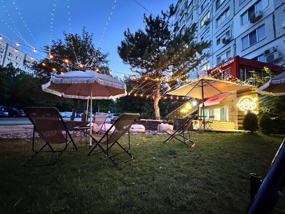Outdoor terrace with umbrellas and seating in evening light, adjacent building visible