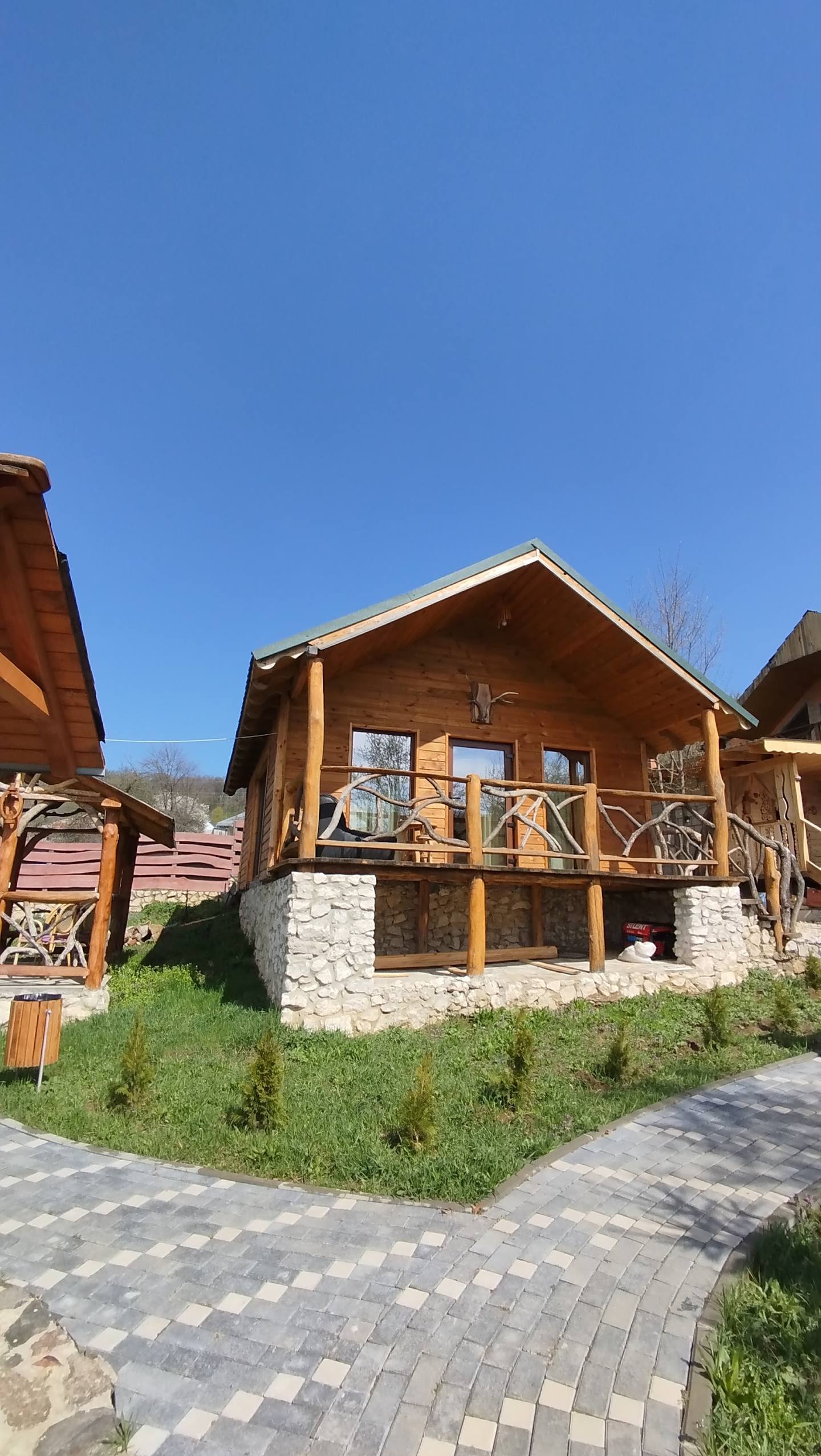 Wooden lodge cabin with stone foundation and paved entrance, set in hillside grounds.