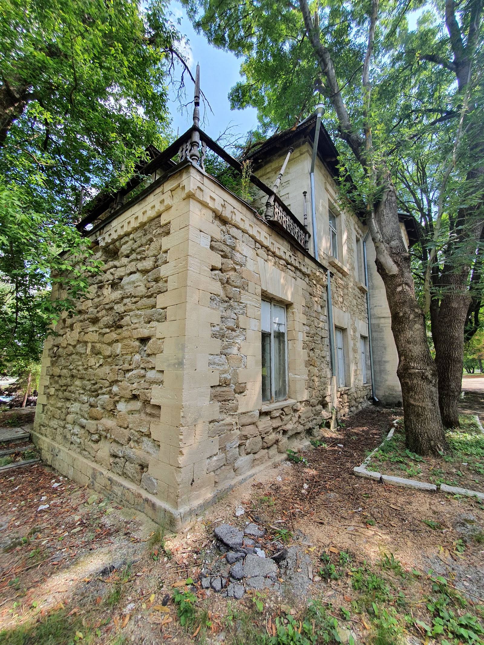 Historic stone manor house with pitched roof surrounded by mature trees