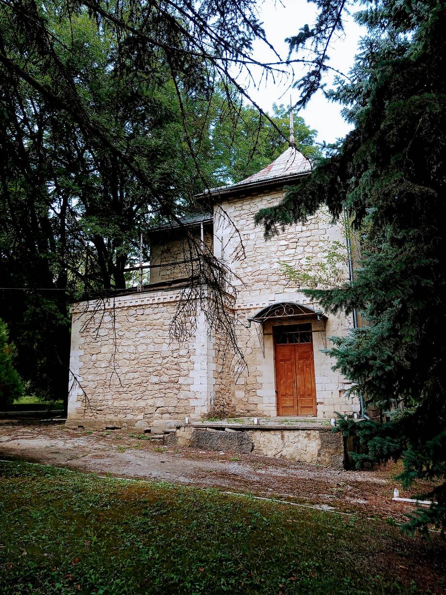 Historic stone monastery with red door framed by mature trees