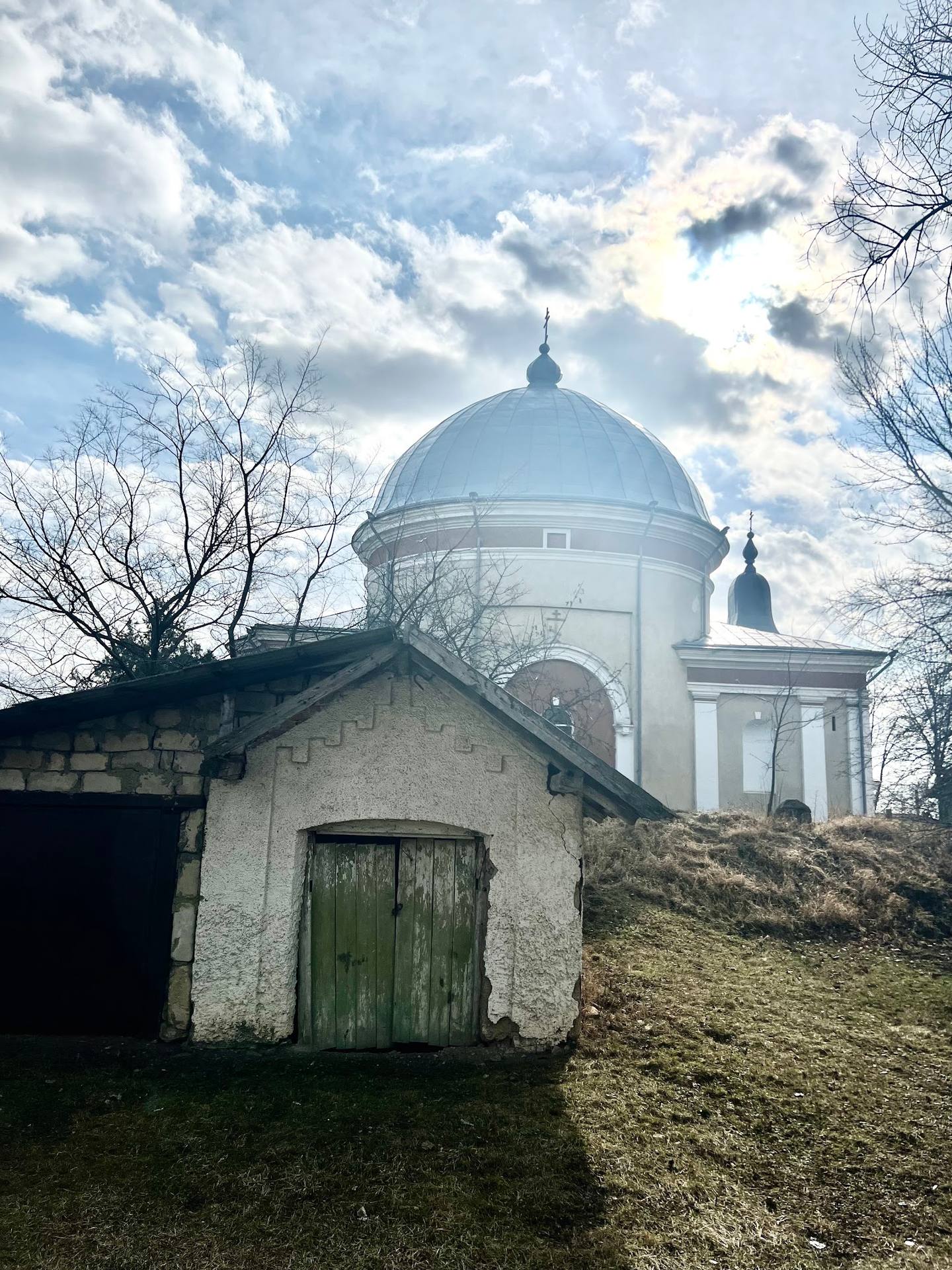 Monastery with white dome and bell tower against sky, foreground cottage ruins