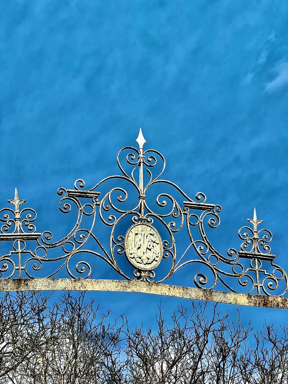 Ornate wrought-iron gate crown with clock detail against blue sky