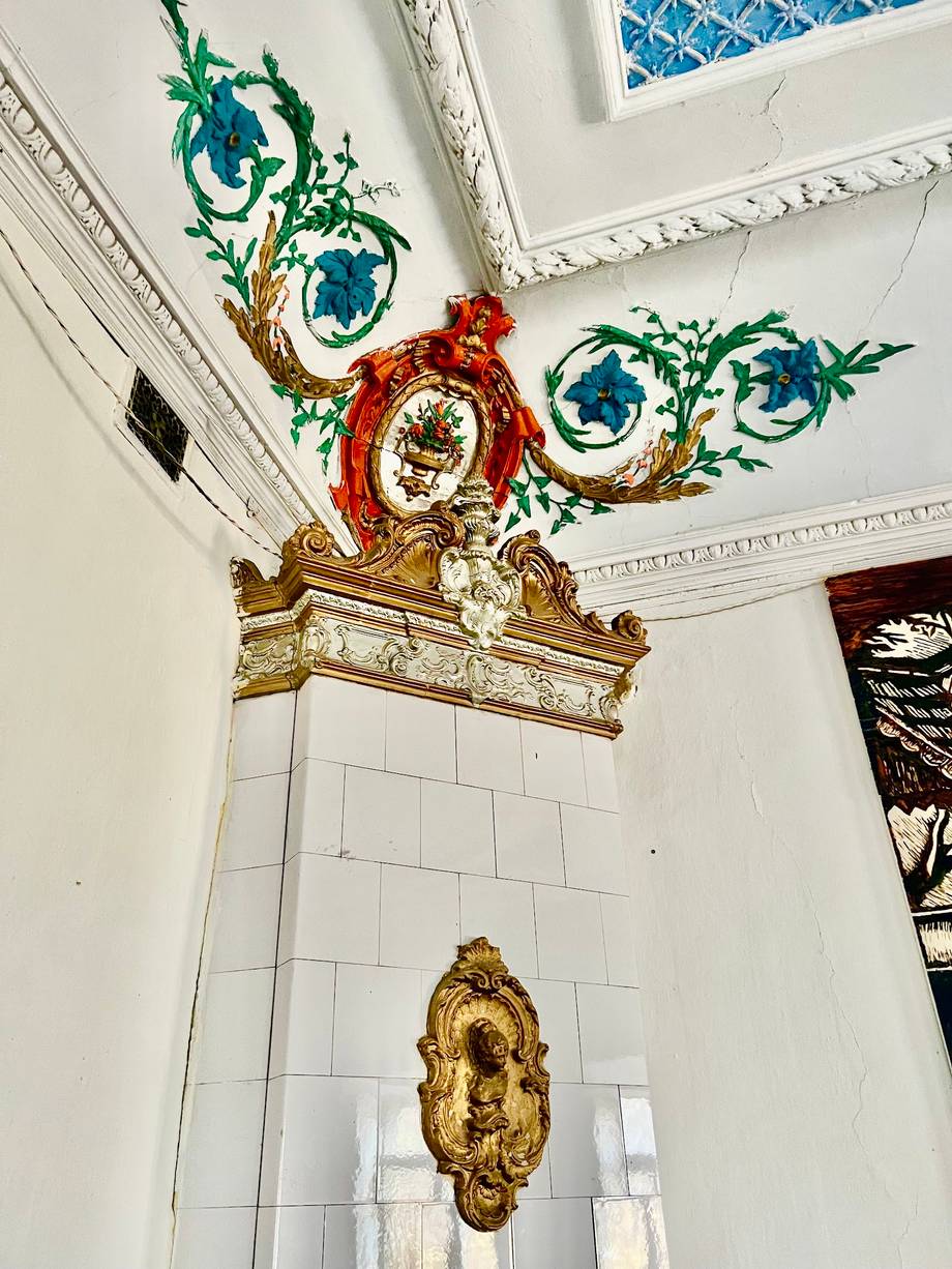 Ornate ceiling decorations with baroque sculptural elements and blue botanical motifs in white interior