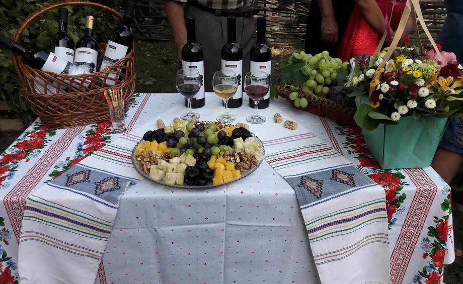 Wine and cheese tasting display with bottles, grapes, and decorative linens outdoors