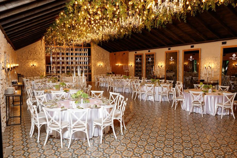 Grand banquet hall with warm amber lighting, soaring ceiling with hanging florals, and elegantly set round tables with white chairs