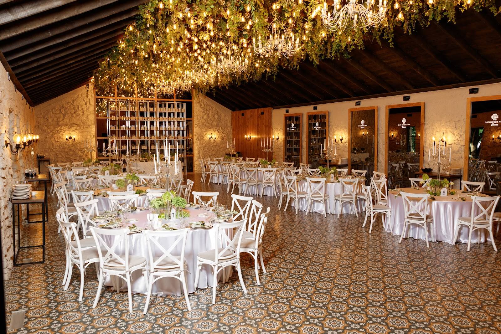 Grand banquet hall with warm amber lighting, soaring ceiling with hanging florals, and elegantly set round tables with white chairs