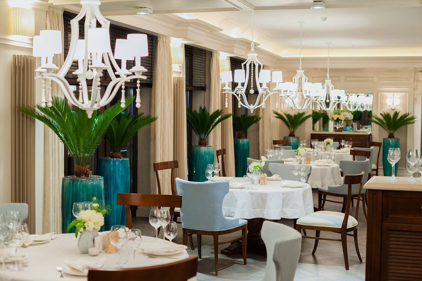 Elegant banquet hall with white chandeliers, teal floral arrangements, and round dining tables set for events