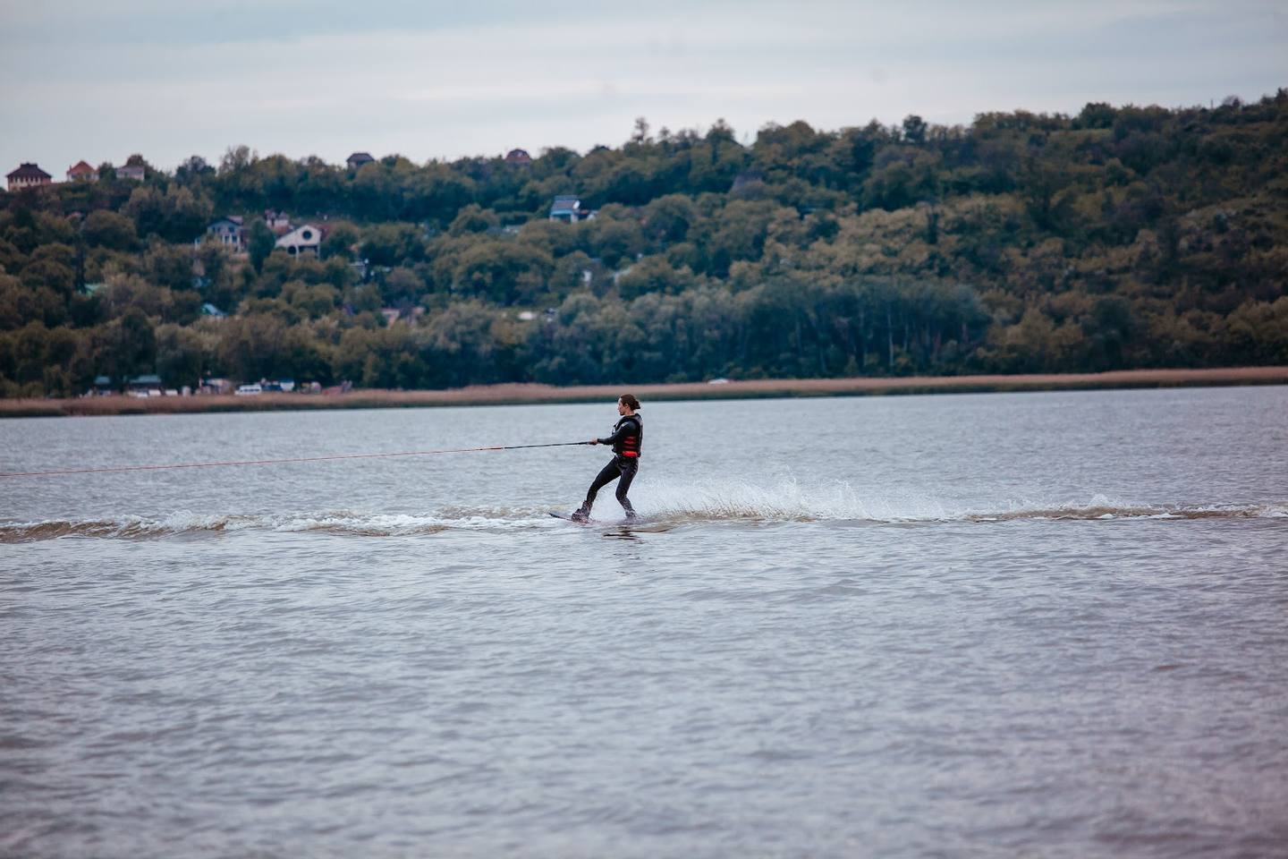 Wading in natural water body with forested hills and residential homes in background