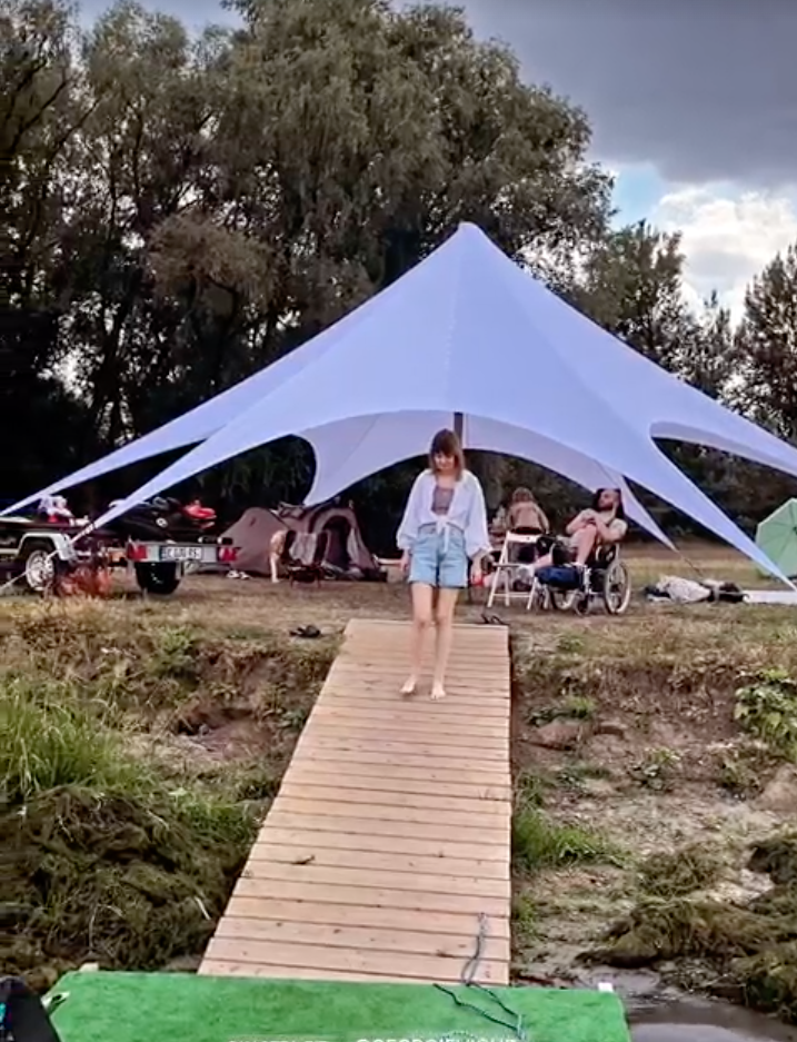 Glamping tent with wooden boardwalk and forest backdrop, guests gathered for outdoor event