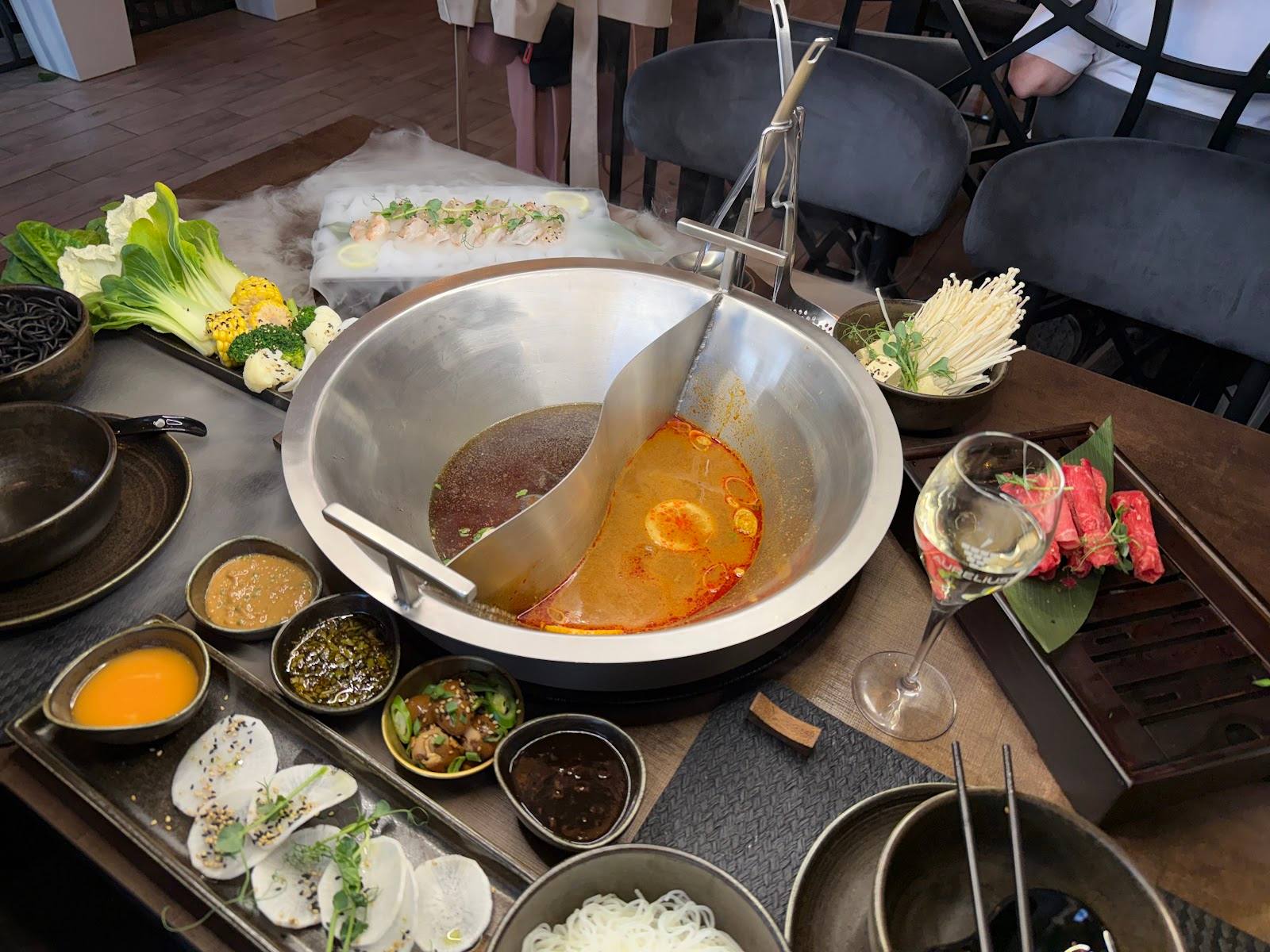 Hot pot dining setup with broth, fresh ingredients, and sauce bowls at table