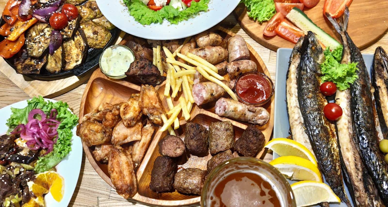 Overhead spread of grilled meats, seafood, fries, and seasonal salads on wooden table
