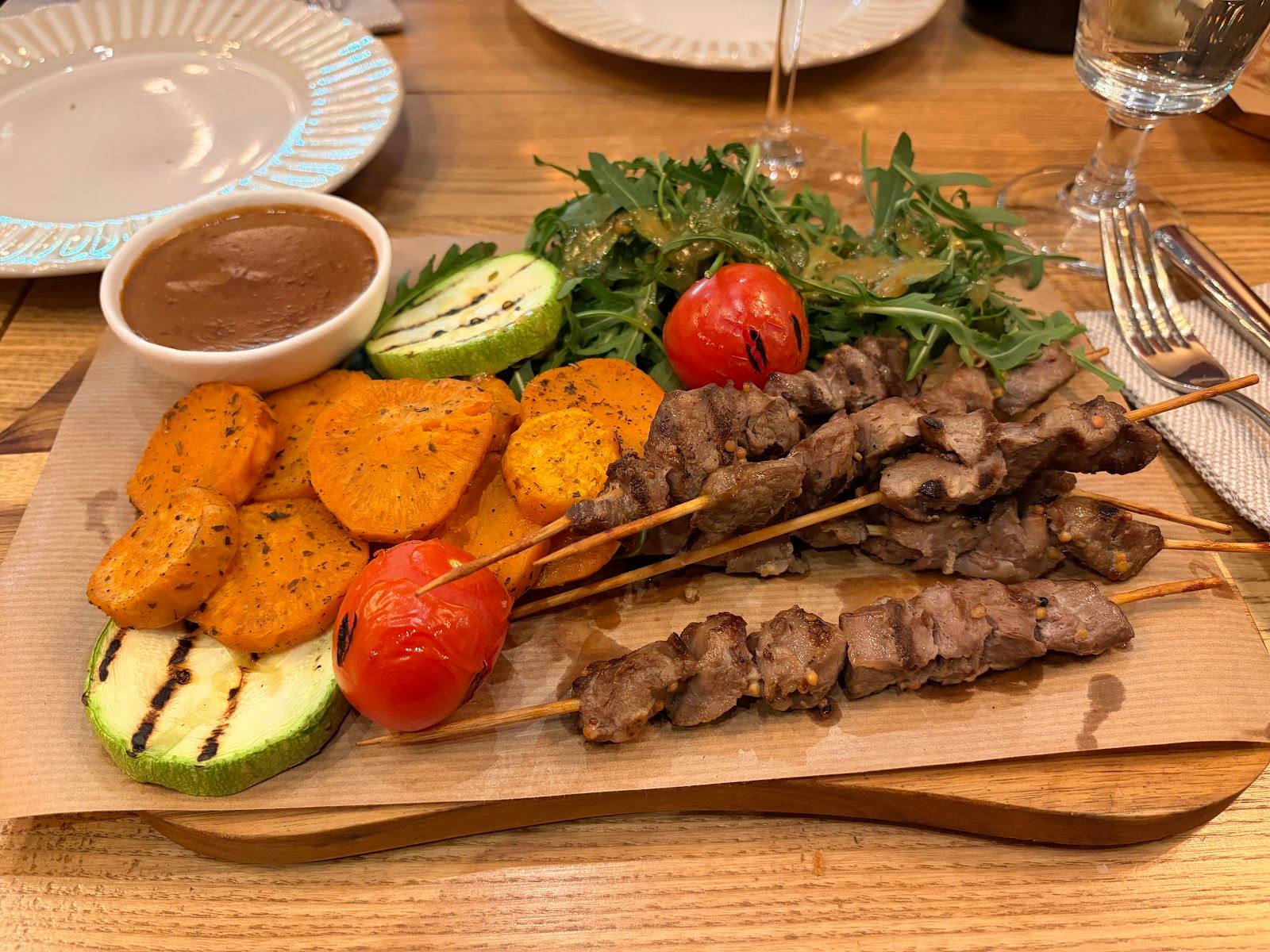 Grilled meat and vegetable platter with dipping sauce on wooden board