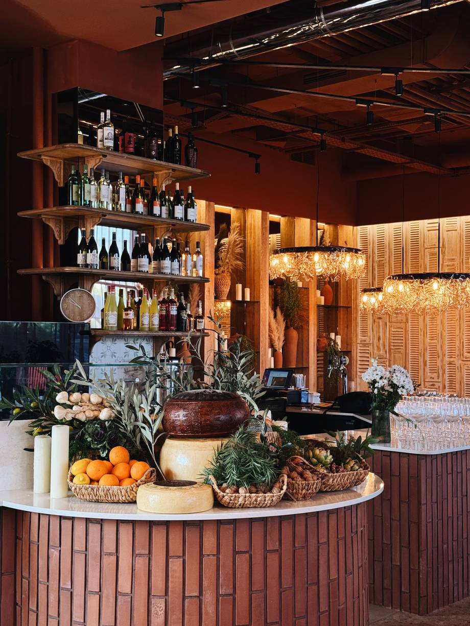 Wine bar counter with shelved bottles, warm amber lighting, and artfully arranged fresh produce display