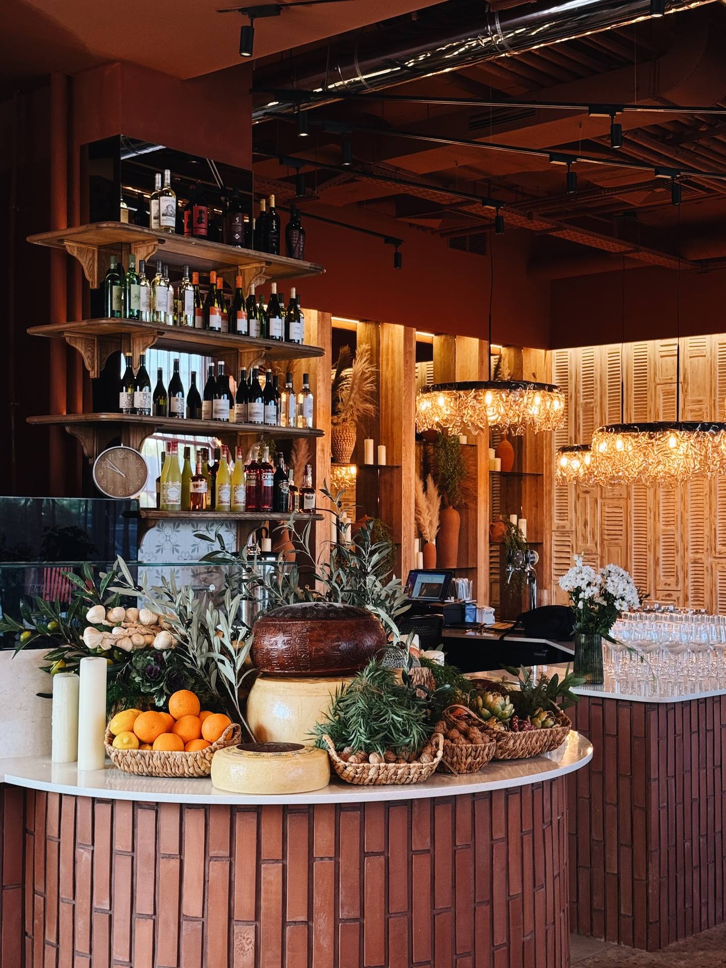 Wine bar counter with shelved bottles, warm amber lighting, and artfully arranged fresh produce display