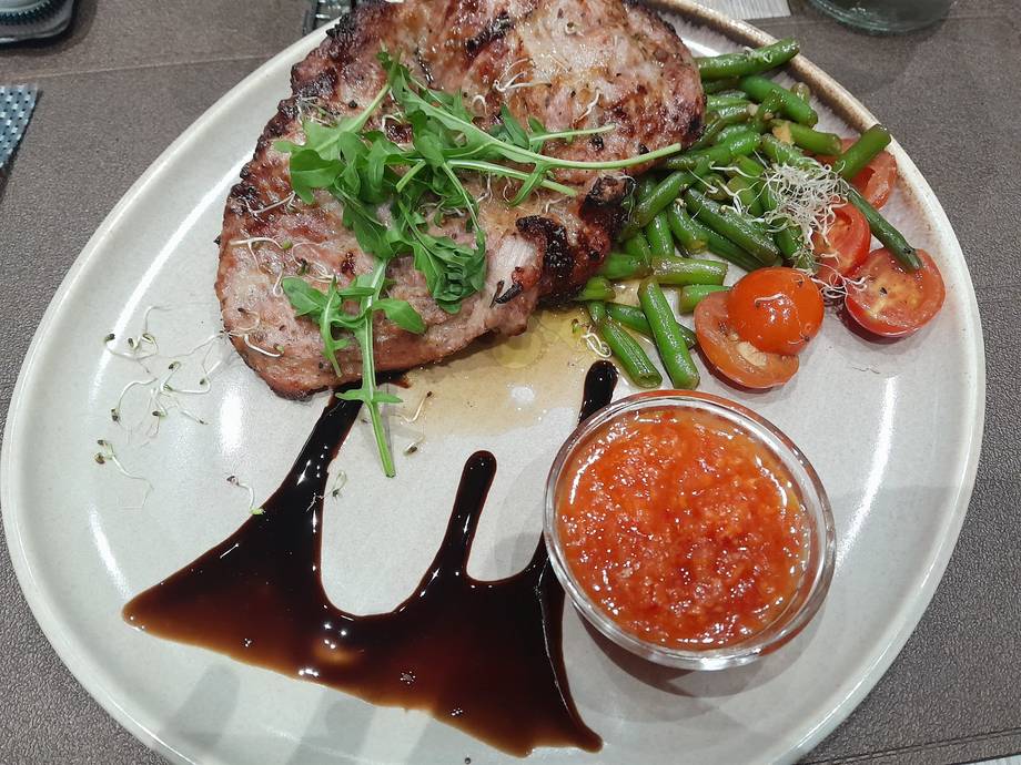 Plated meat dish with greens and tomato relish on white dinnerware