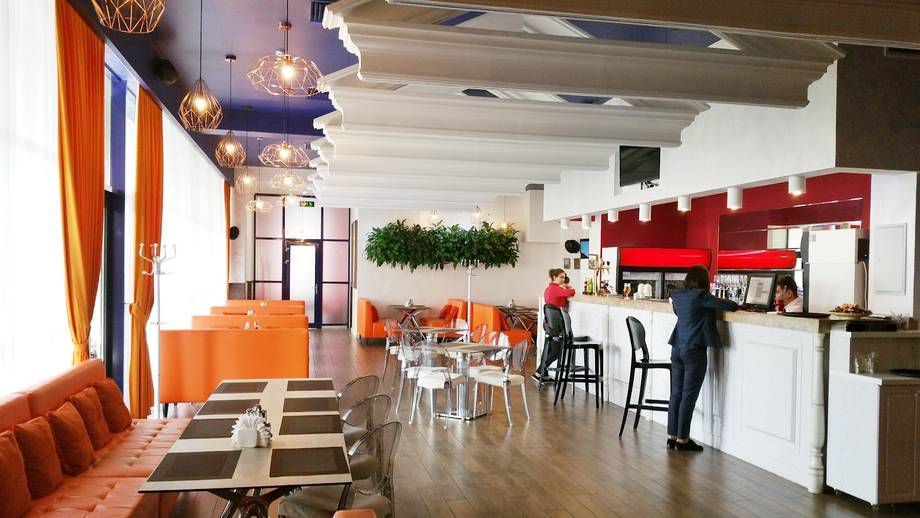 Modern cafe interior with orange accents, dining area, and open kitchen