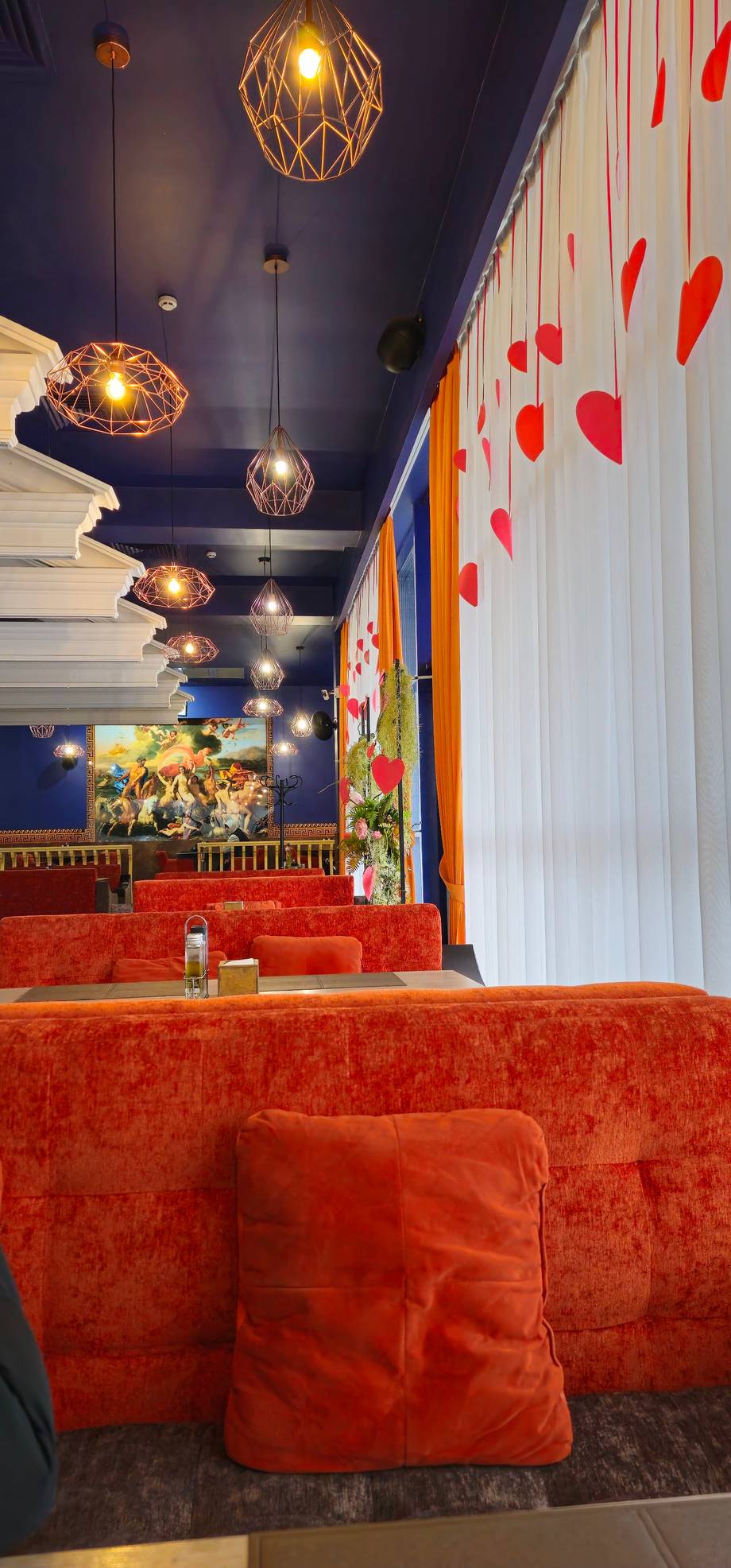 Modern cafe interior with geometric pendant lights, red velvet seating, and decorative wall installations