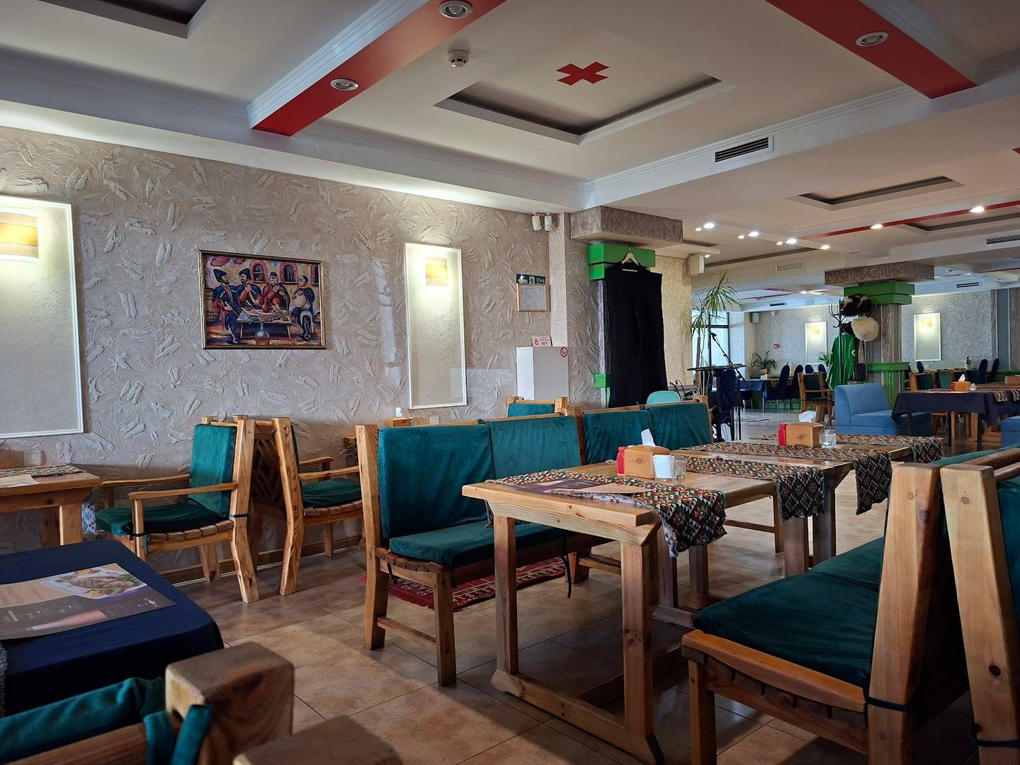 Modern restaurant interior with wood tables, teal upholstered seating, and contemporary ceiling design