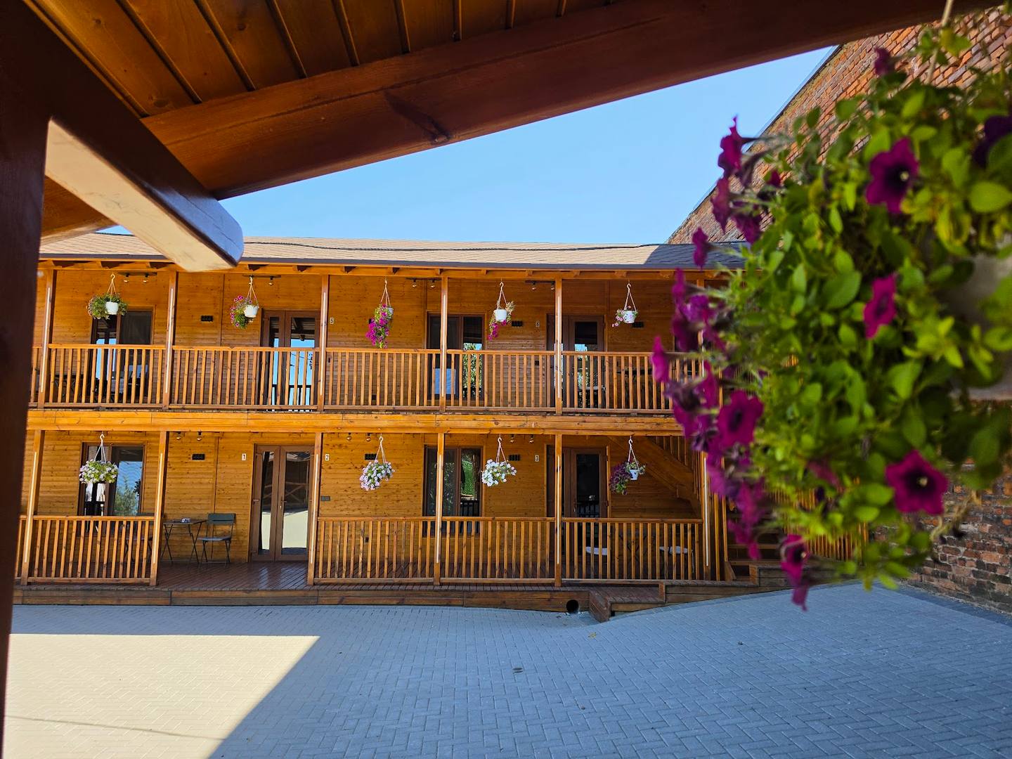 Two-story wooden timber building with covered terrace, bright courtyard, and flowering climbing ivy.