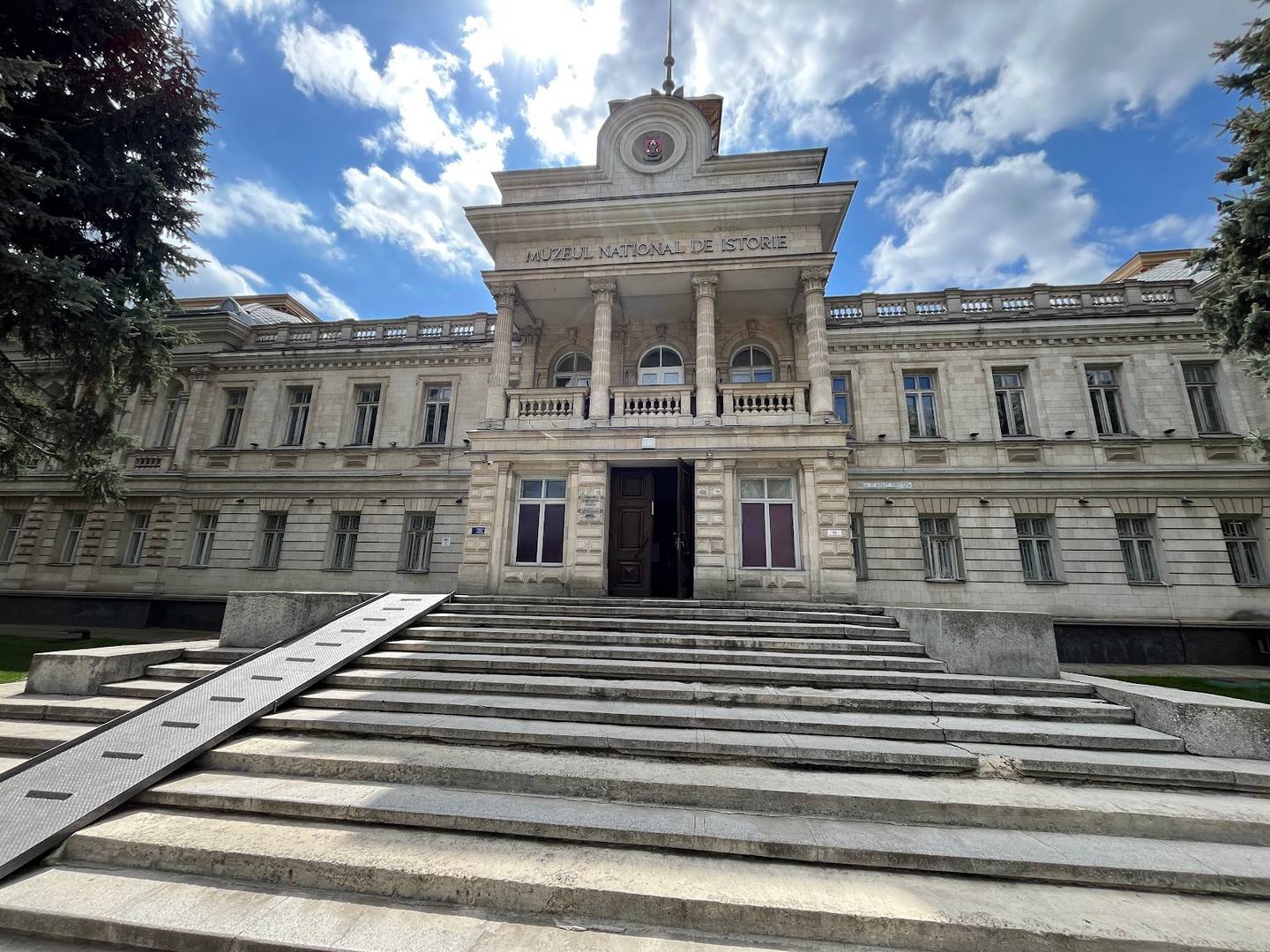 Grand neoclassical facade with columns and clock tower, formal stone steps
