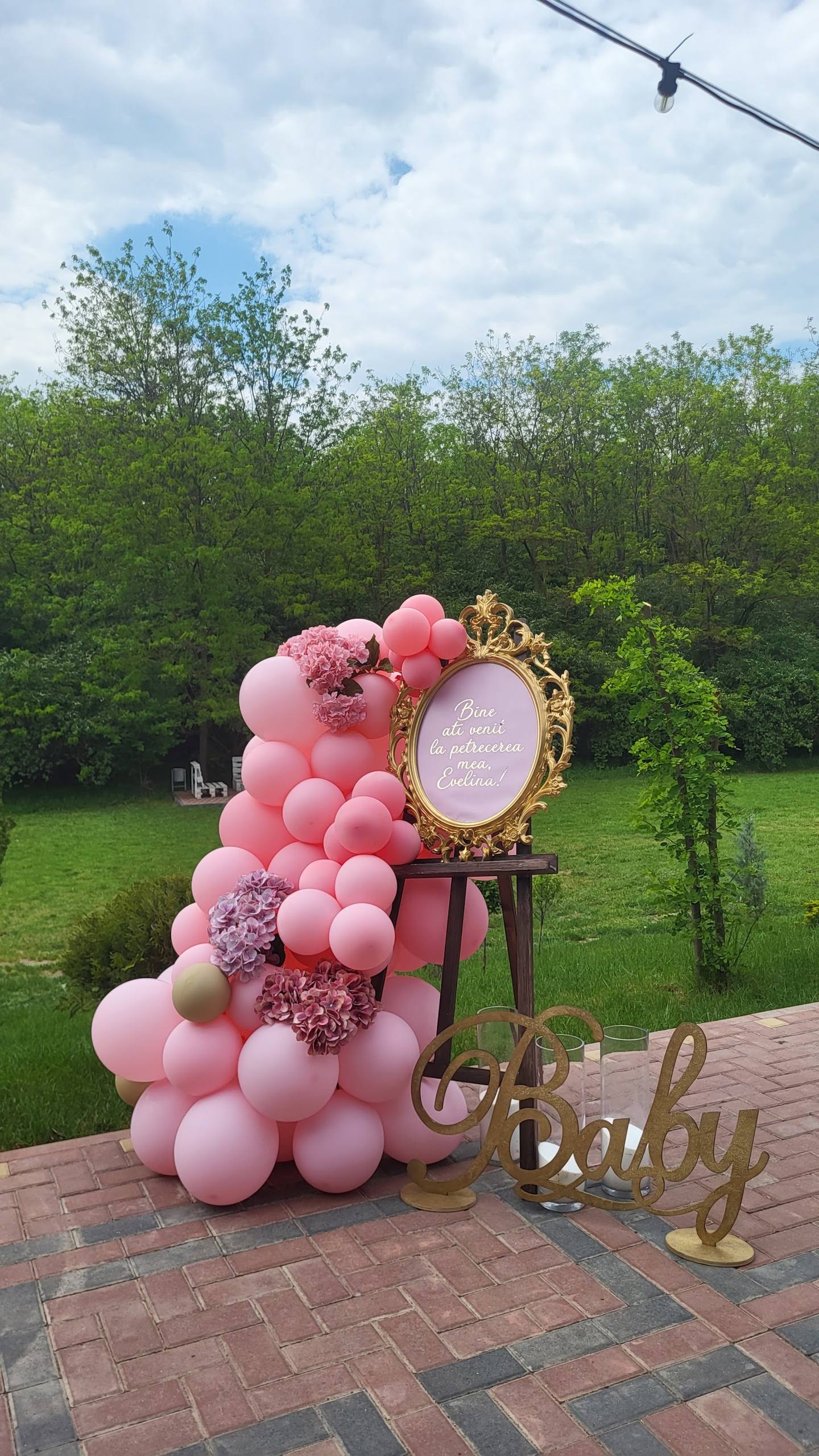 Pink balloon installation and decorative signage on brick patio with rural backdrop