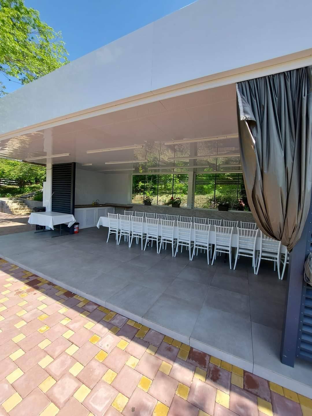Modern covered terrace with white seating, retractable curtain, and manicured grounds