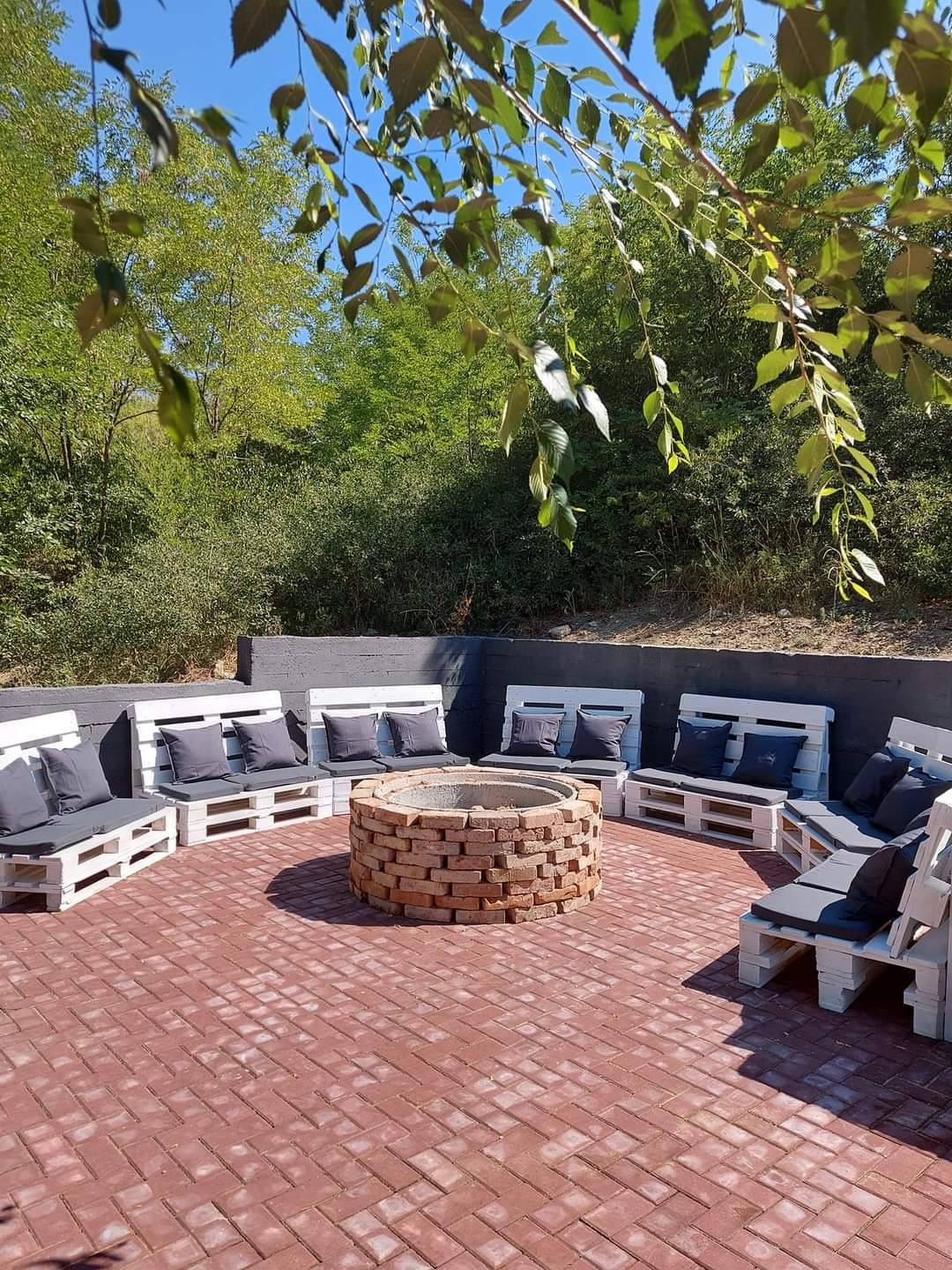 Outdoor terrace with brick patio, circular fire pit, and comfortable seating area surrounded by trees