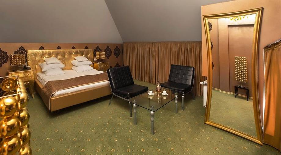Hotel room with golden-brown décor, wooden bed frame, and modern amenities at angled ceiling