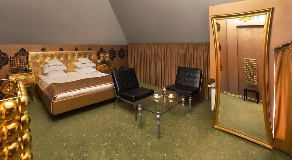 Hotel room with golden-brown décor, wooden bed frame, and modern amenities at angled ceiling