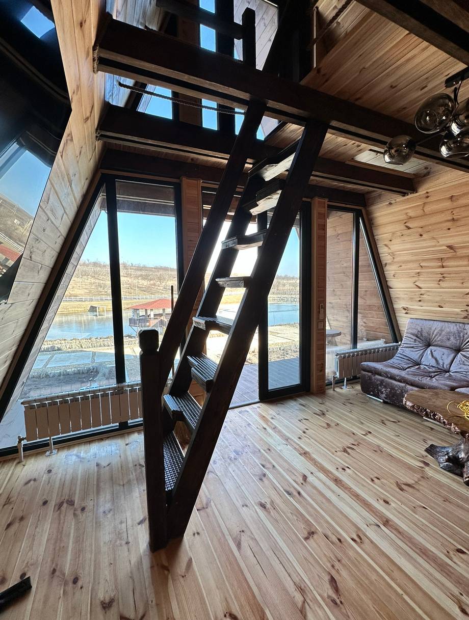 Modern wooden interior with panoramic windows overlooking water and hillside landscape