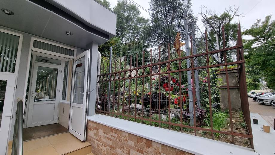 Storefront entrance with white facade and decorative metal gate with flowering vines