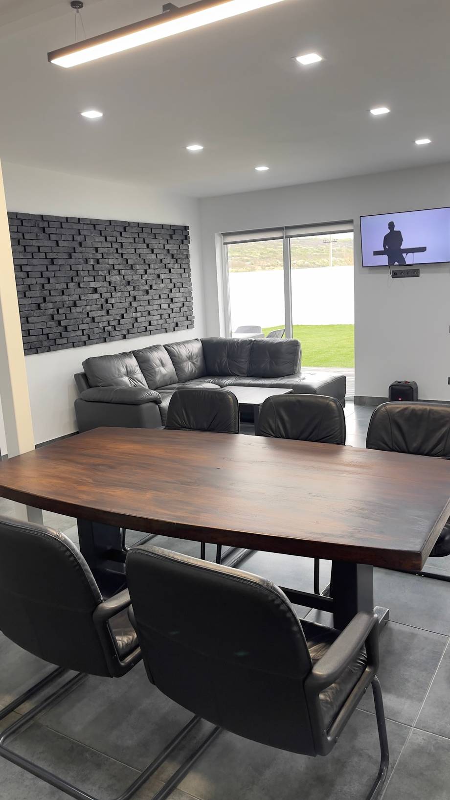 Modern meeting room with wood conference table, grey lounge seating, and garden views