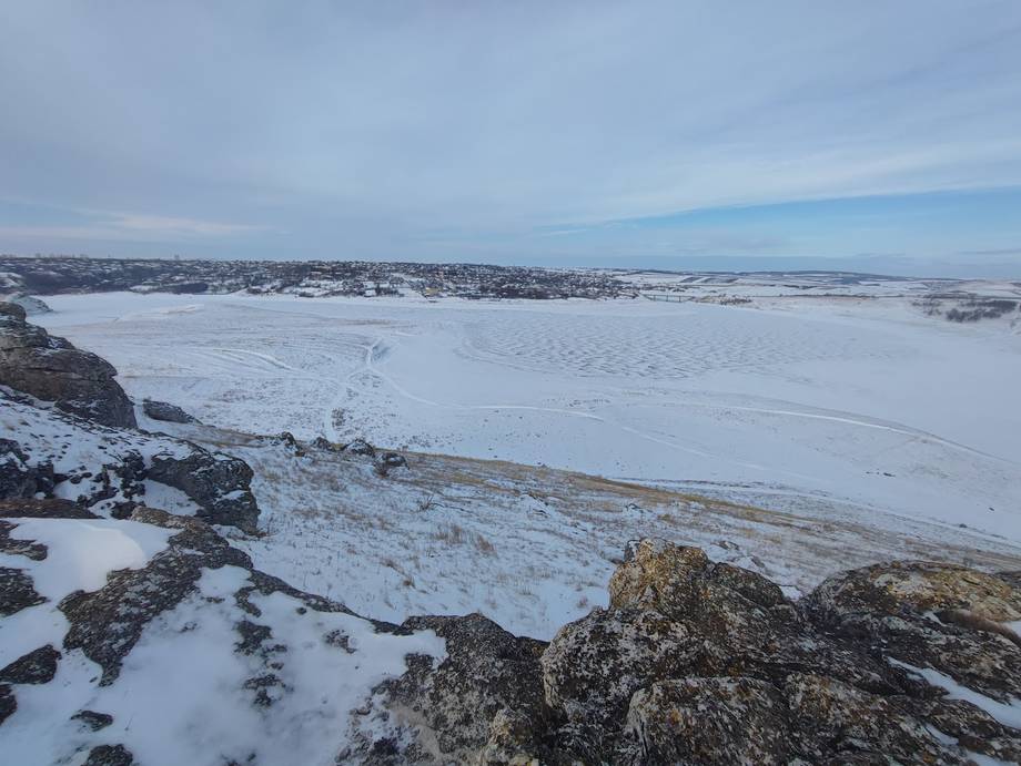 Winter landscape with frozen water body and distant town settlement across snowy terrain