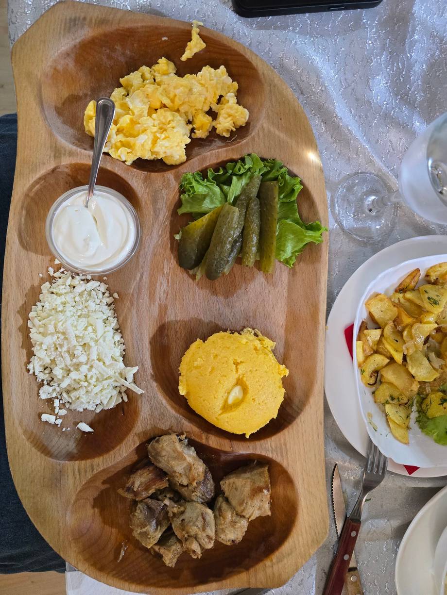 Wooden board with appetizer sampler featuring egg salad, pickles, cheese, meats and sauce