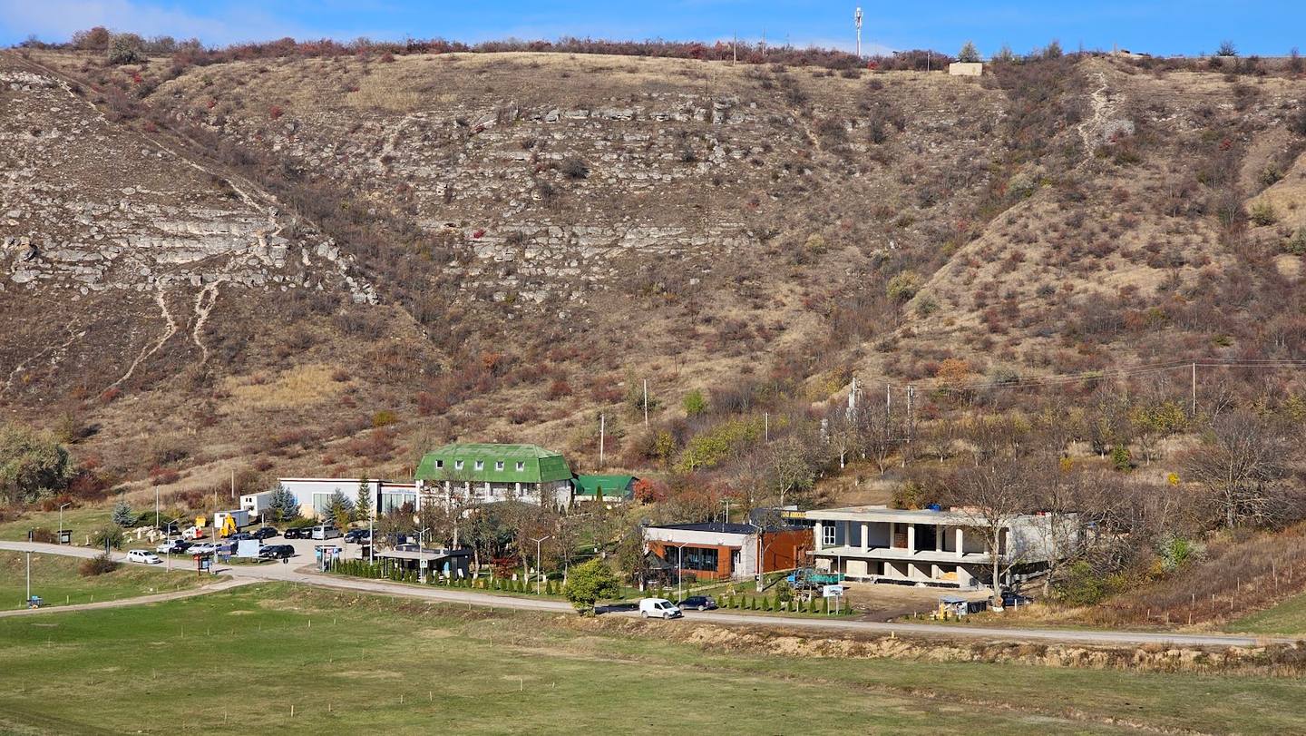 Rural winery or agritourism venue nestled at the foot of vineyard-covered hillside with guest buildings and terraced grounds