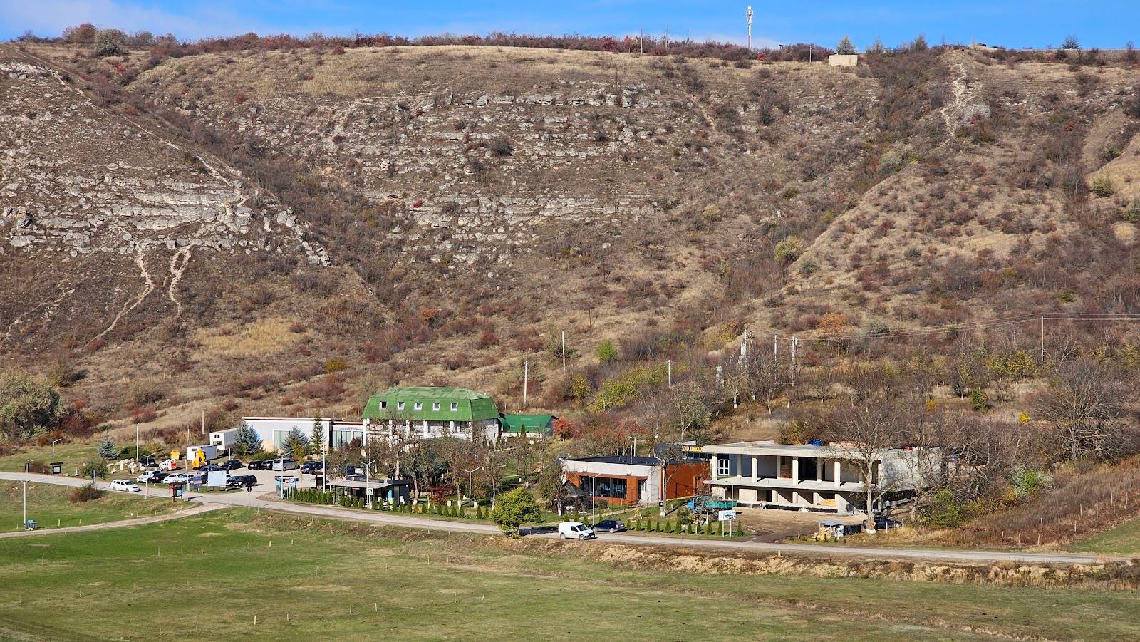 Rural winery or agritourism venue nestled at the foot of vineyard-covered hillside with guest buildings and terraced grounds