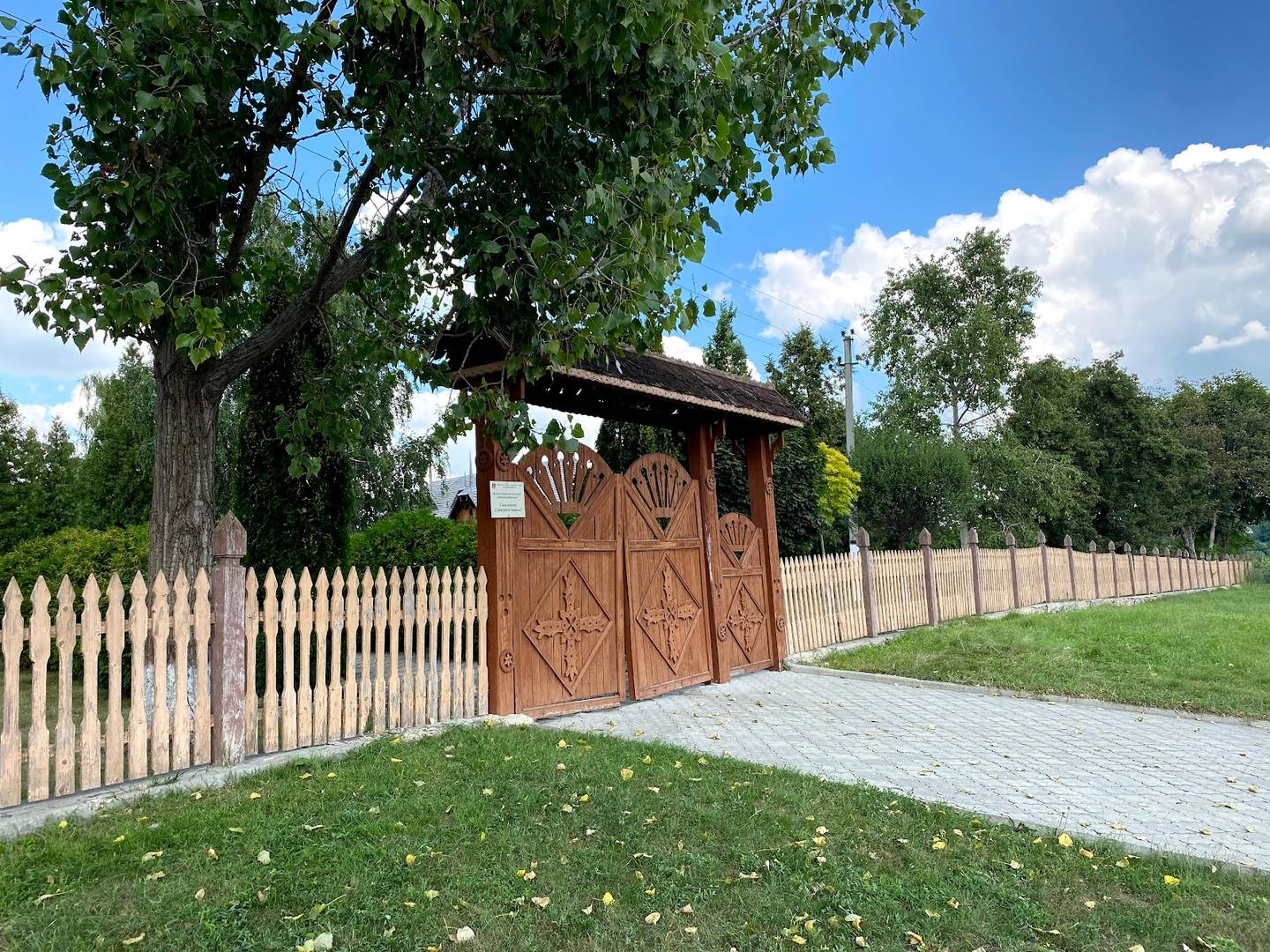 Traditional wooden gate with white fence and ancient oak tree at monastery entrance