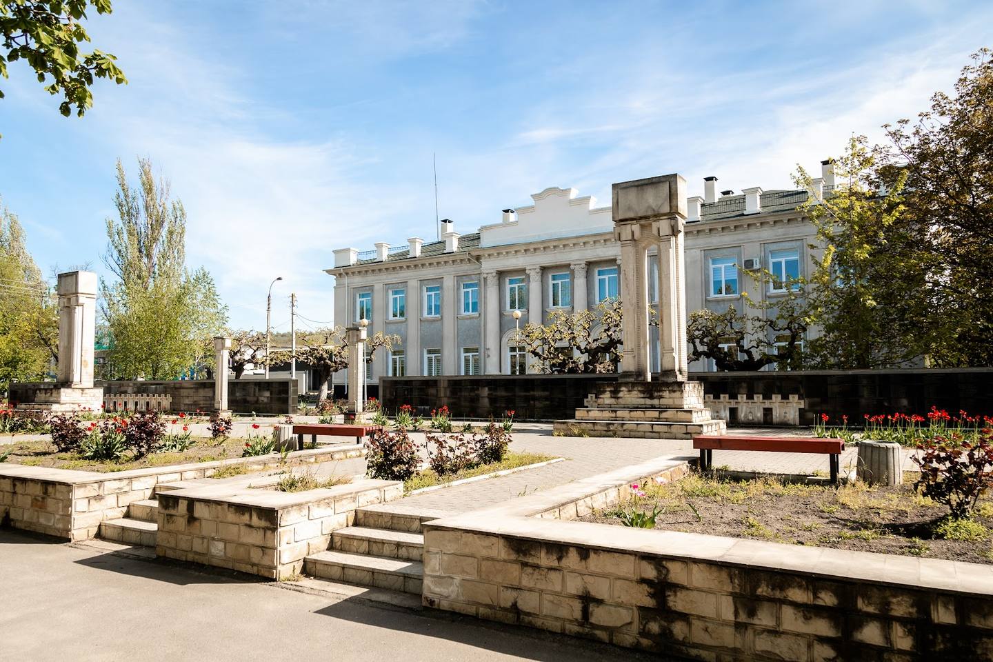 Neoclassical institutional building with blue façade overlooking manicured public square and gardens