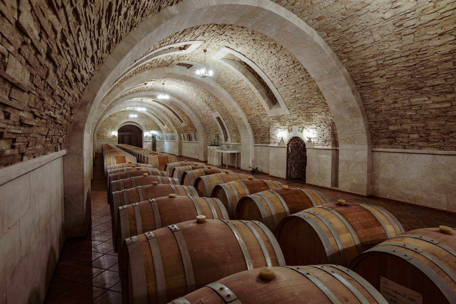 Arched brick cellar with rows of wooden wine barrels aging in temperature-controlled storage