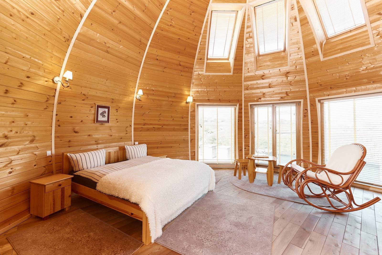 Wooden dome bedroom with skylight windows, bed, and lounge chair in geodesic interior
