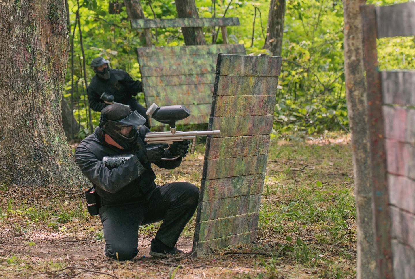 Player aiming paintball marker at wooden target in outdoor woodland arena