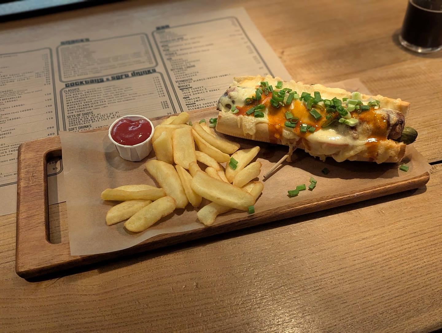 Plated hot dog with fries and sauce on wooden serving board