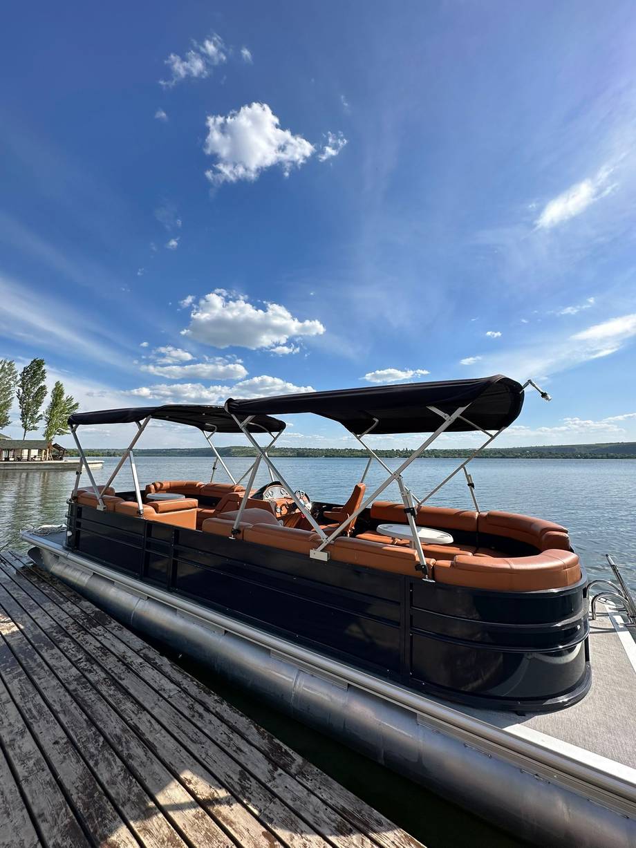 Pontoon boat docked at waterfront with clear lake view and blue sky