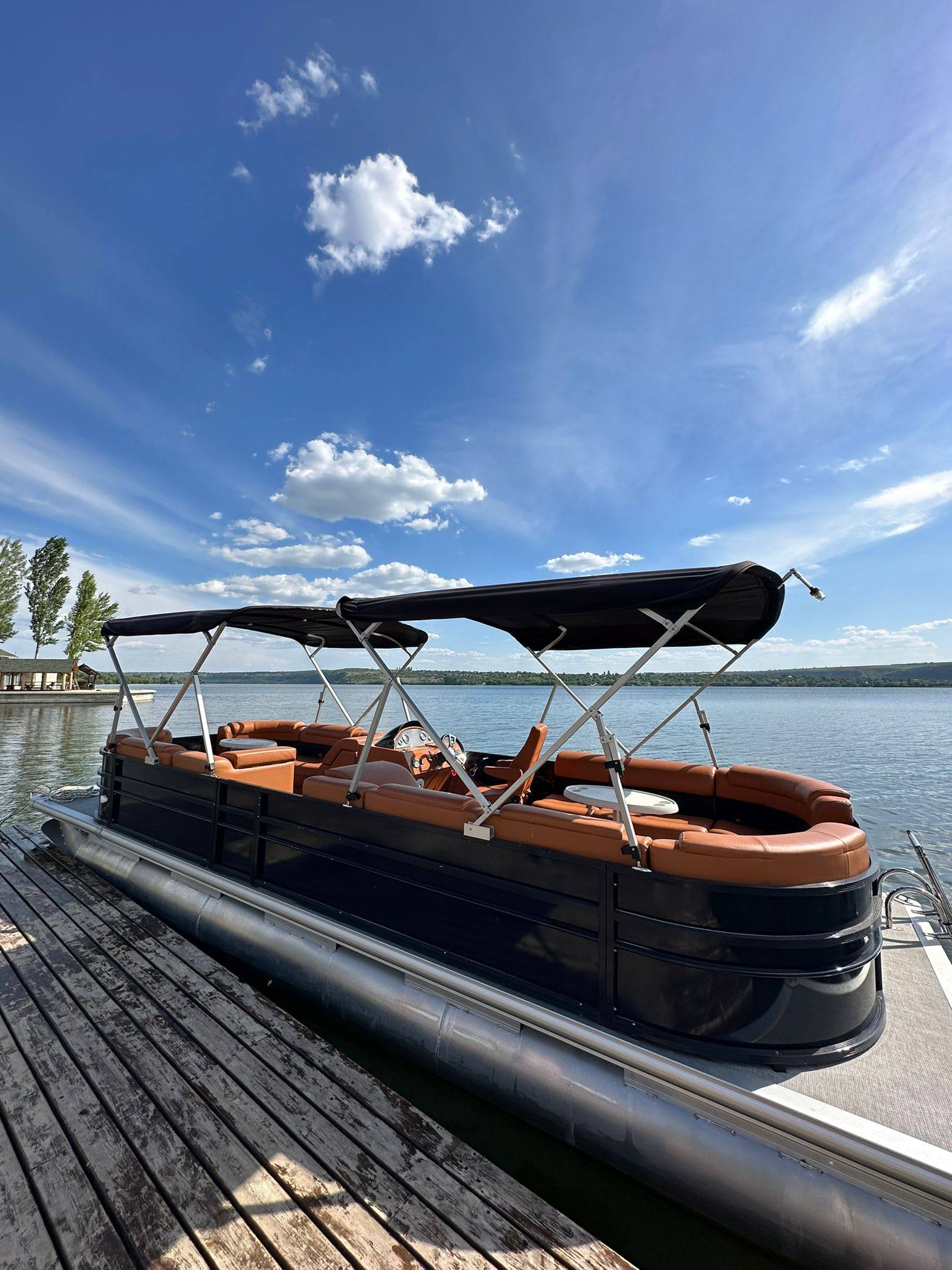 Pontoon boat docked at waterfront with clear lake view and blue sky