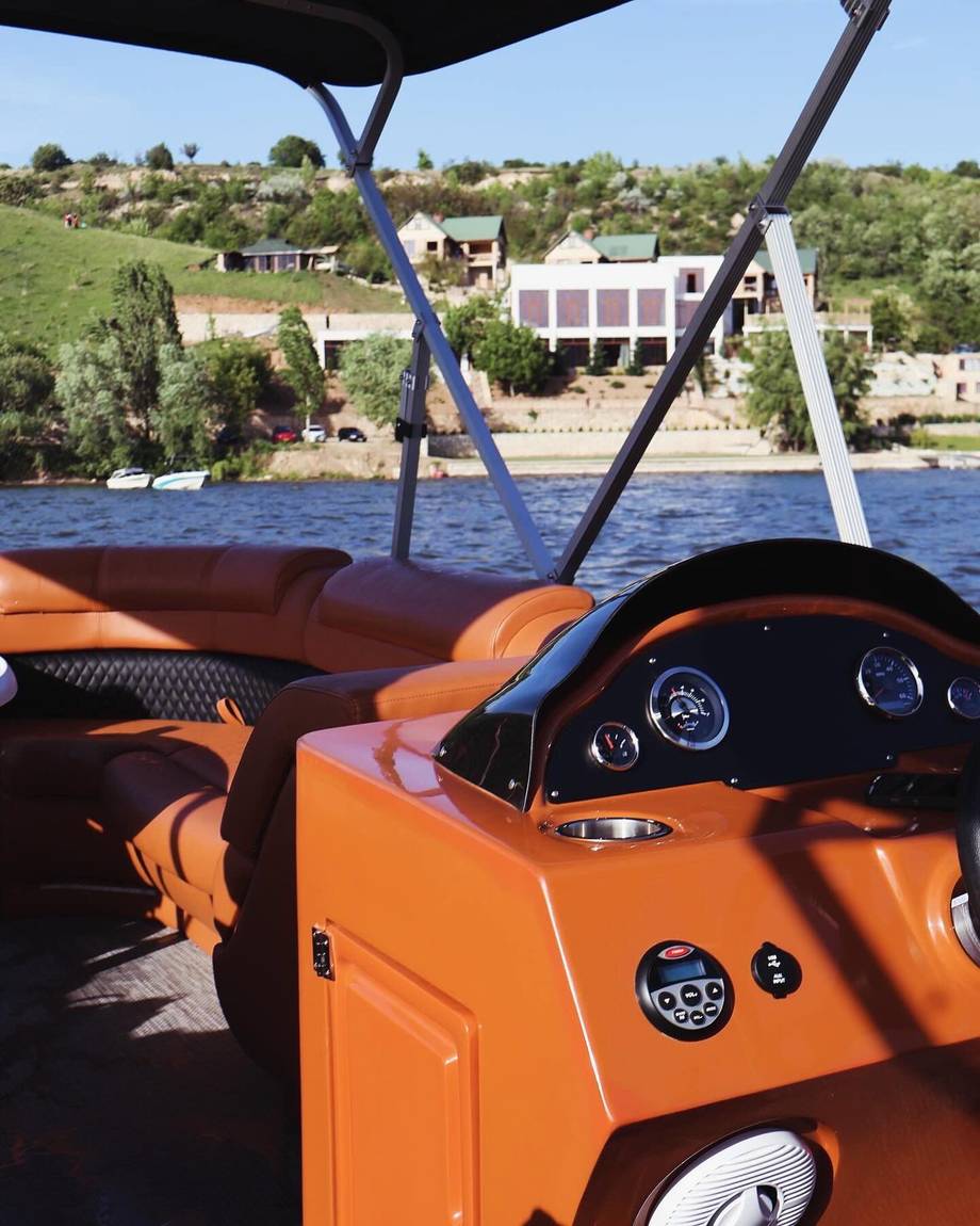 Orange speedboat with control console on river, waterfront property visible