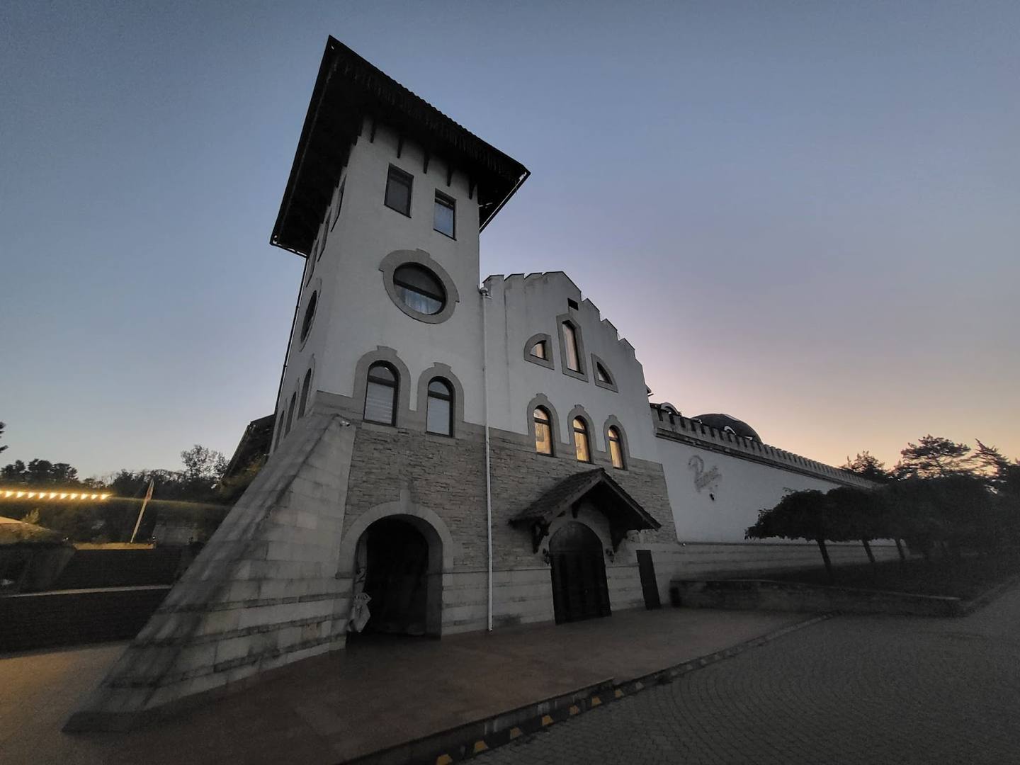 White stone monastery building with distinctive tower and arched entrances at dusk
