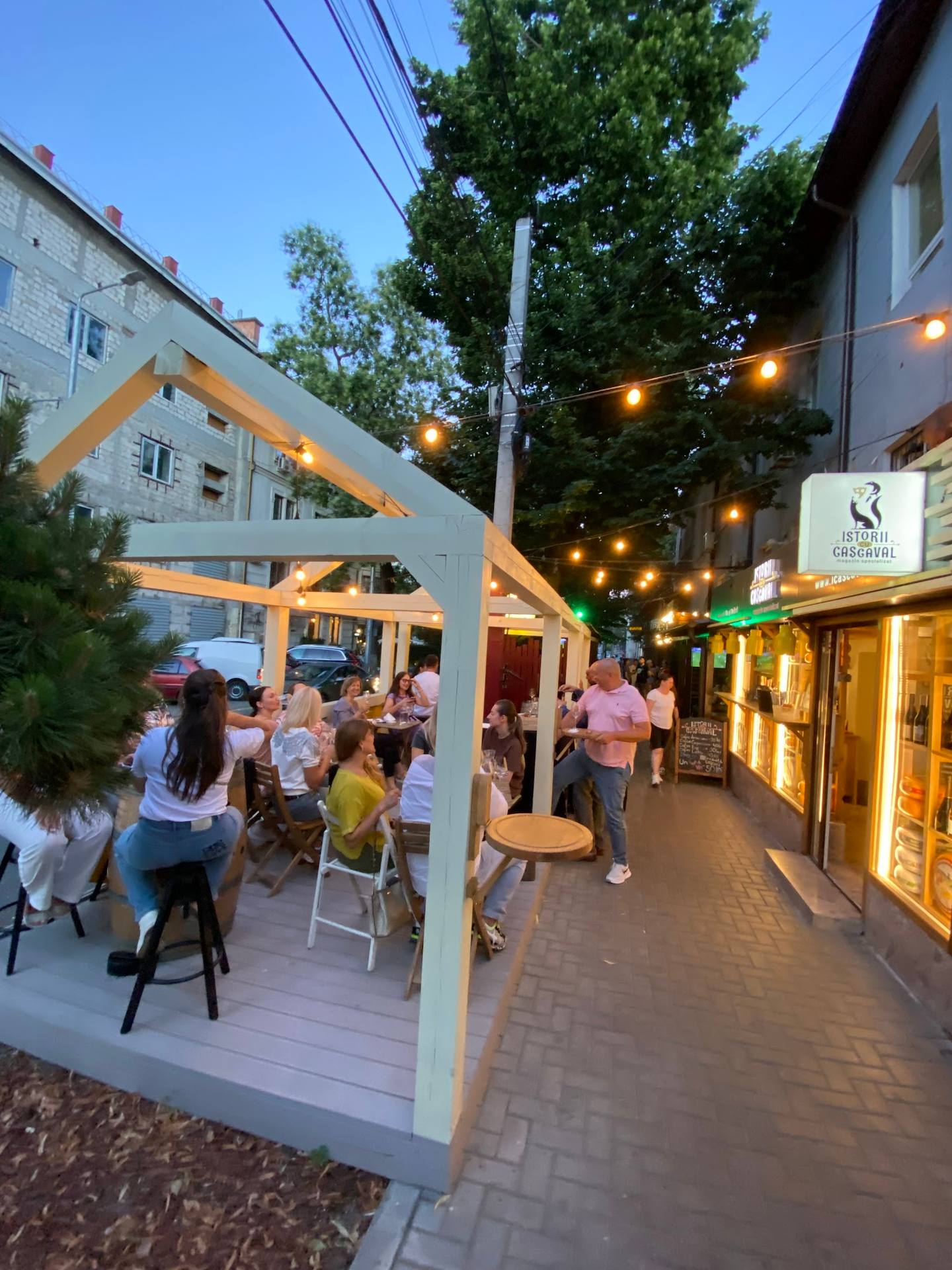 Evening terrace and street view with lit pavilion and guests enjoying outdoor dining