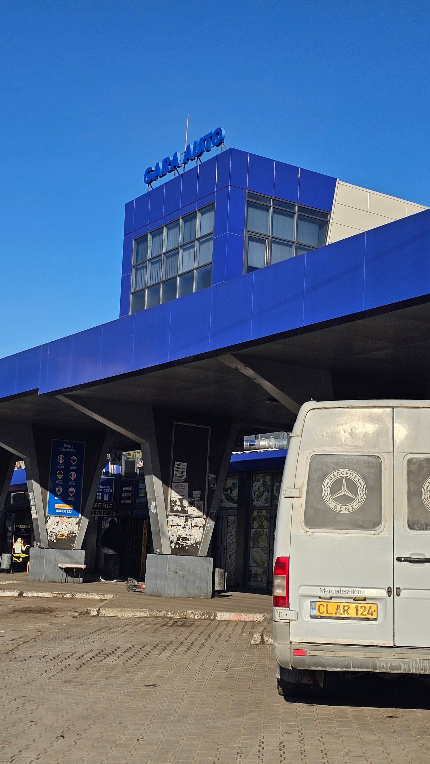 Blue modern storefront with signage under clear sky, service vehicles parked at entrance