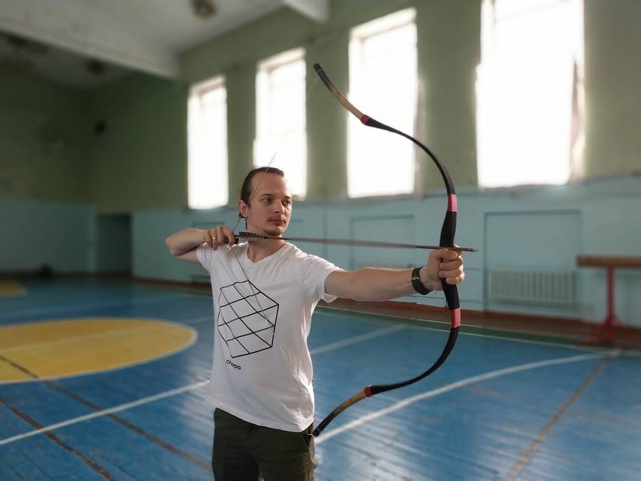 Archer drawing bow in indoor sports hall with blue court flooring