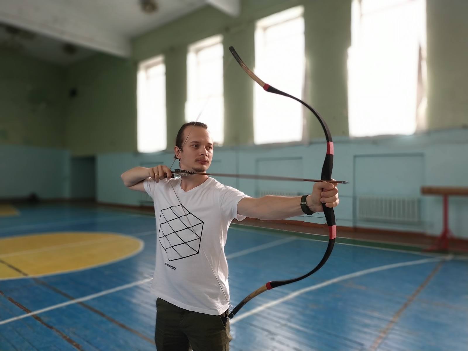 Archer drawing bow in indoor sports hall with blue court flooring